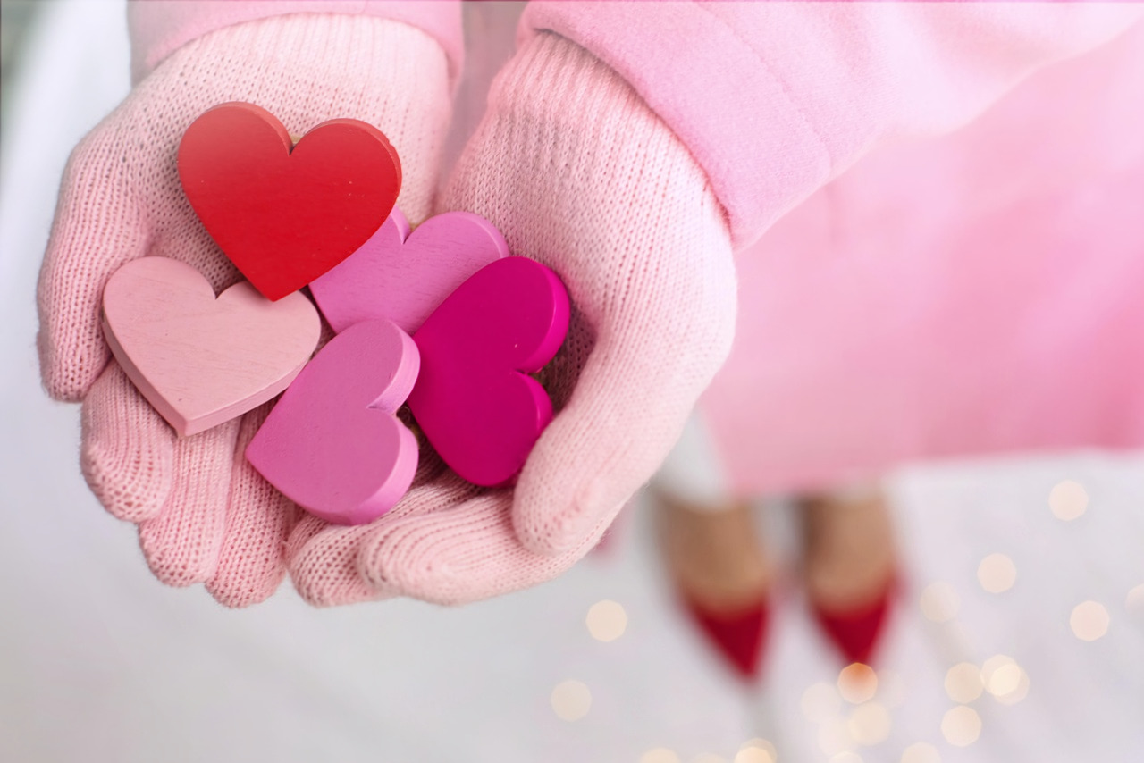 A woman's hands wearing pink gloves offering hearts in various shades of red and pink